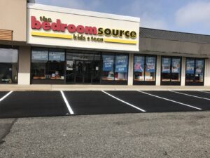 Fresh asphalt repair and line striping completed in front of a retail storefront, creating clean, clearly marked parking spaces.