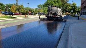 Distributor truck spraying liquid asphalt tack coat on a private commercial road during an early fall paving project