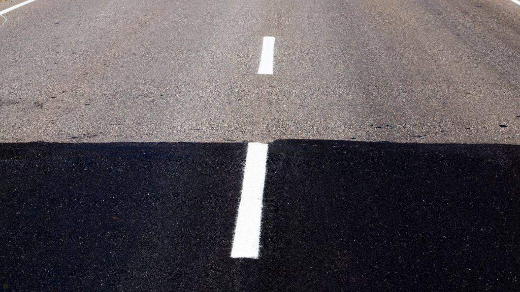Split view comparing an old weathered roadway surface with new dark asphalt and fresh white lane striping
